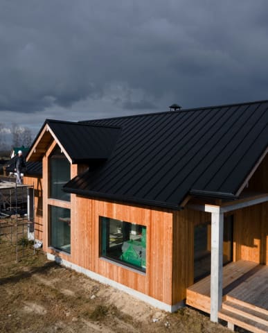 Modern wooden house with black roof under moody sky.